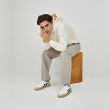 Load image into Gallery viewer, Photo portée d&#39;une baskets vegan confortables avec semelle épaisse. La basket est blanche avec le logo vert