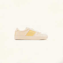 Charger l&#39;image dans la galerie, Vue latérale de la basket posée sur un fond clair, présentant son design épuré et ses détails artisanaux.
La silhouette minimaliste met en valeur la combinaison du tissu beige et des broderies jaunes