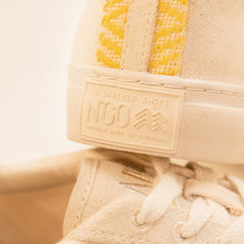 Charger l&#39;image dans la galerie, Gros plan sur l’arrière de la chaussure, mettant en valeur l’inscription en relief &quot;N&#39;GO Vulcanized Shoes, Proudly Made in Vietnam&quot;.
Le détail du tissu beige et du motif jaune brodé est visible le long du talon.
