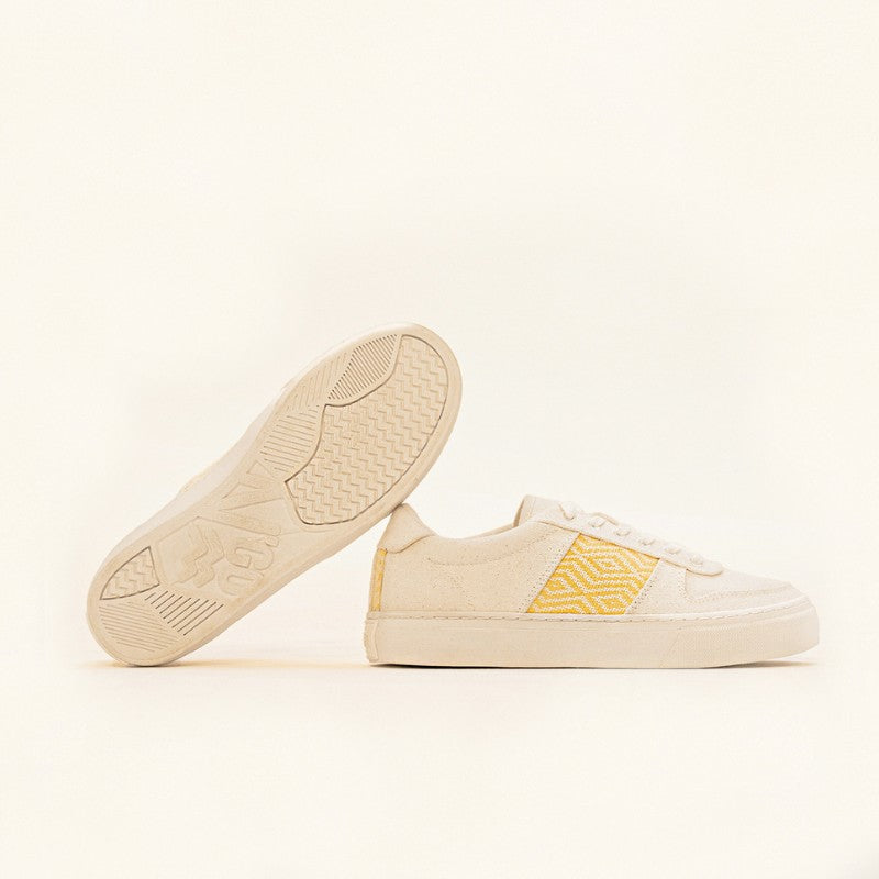Paire de baskets basses en toile beige avec un motif ethnique jaune brodé sur les côtés.
Une chaussure est posée à plat tandis que l&