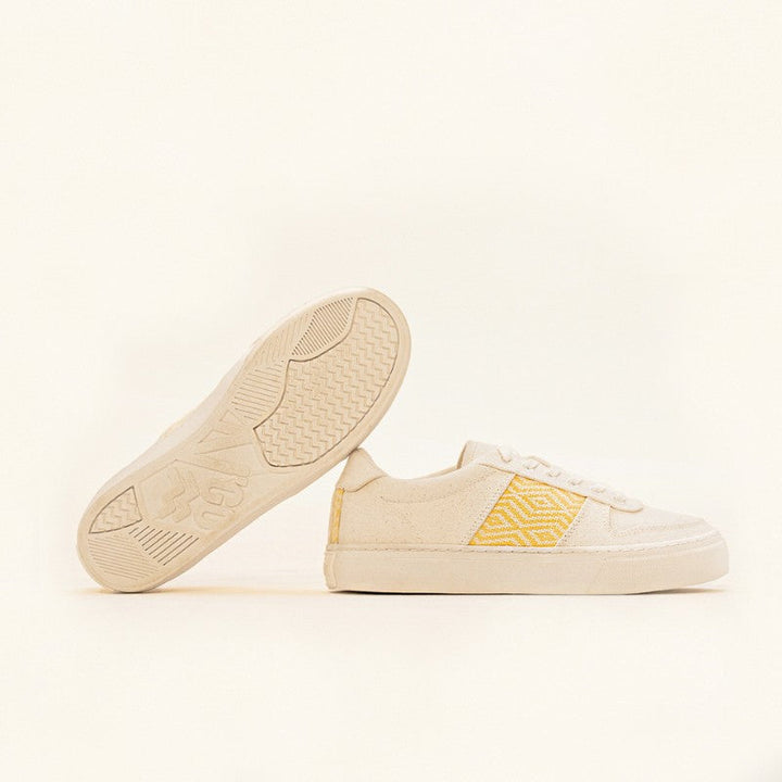 Paire de baskets basses en toile beige avec un motif ethnique jaune brodé sur les côtés.
Une chaussure est posée à plat tandis que l&