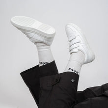 Load image into Gallery viewer, Look casual avec les baskets blanches à scratch Alpha portées, jambes croisées en l’air