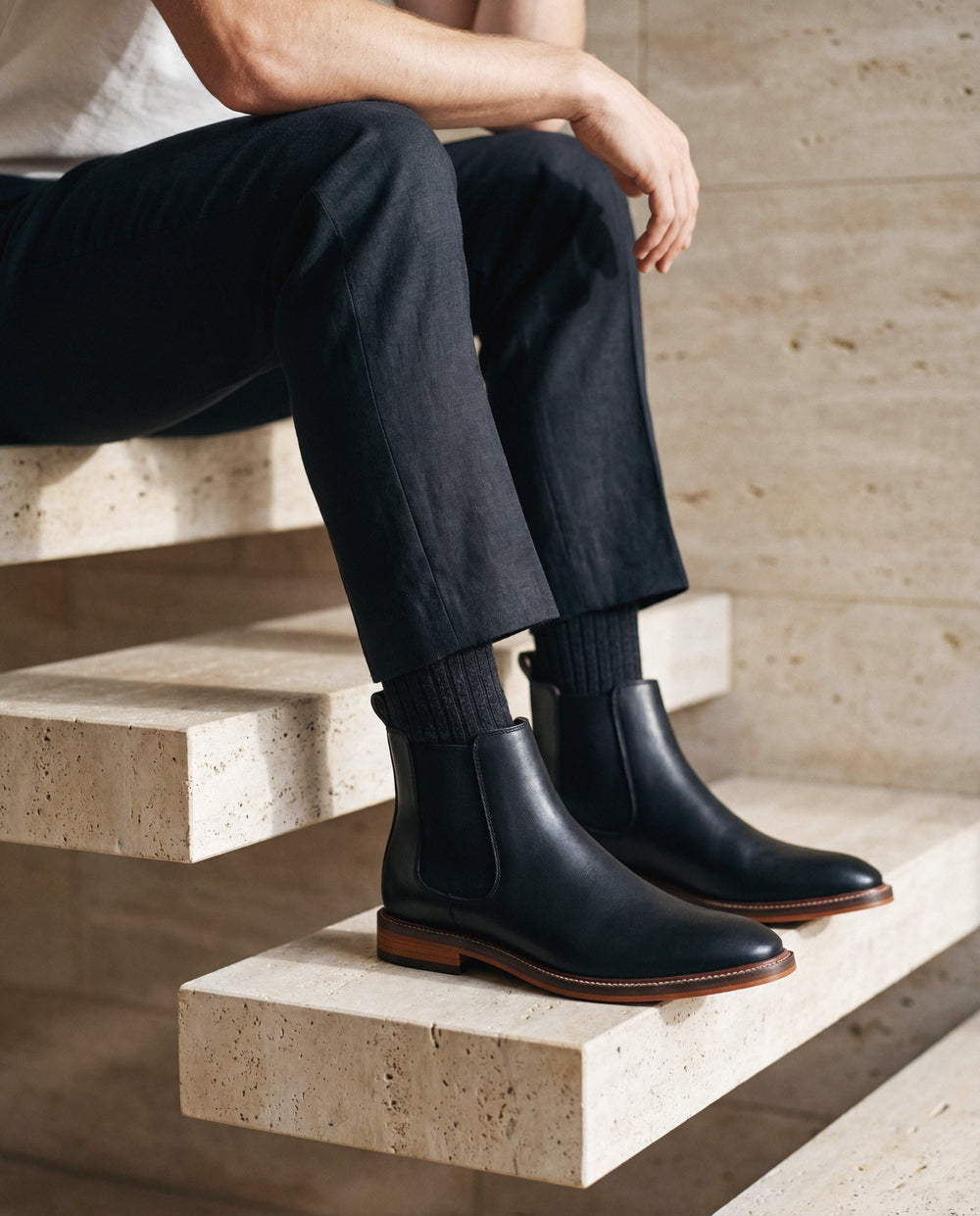 Person wearing black vegan leather boots sitting on stone steps.