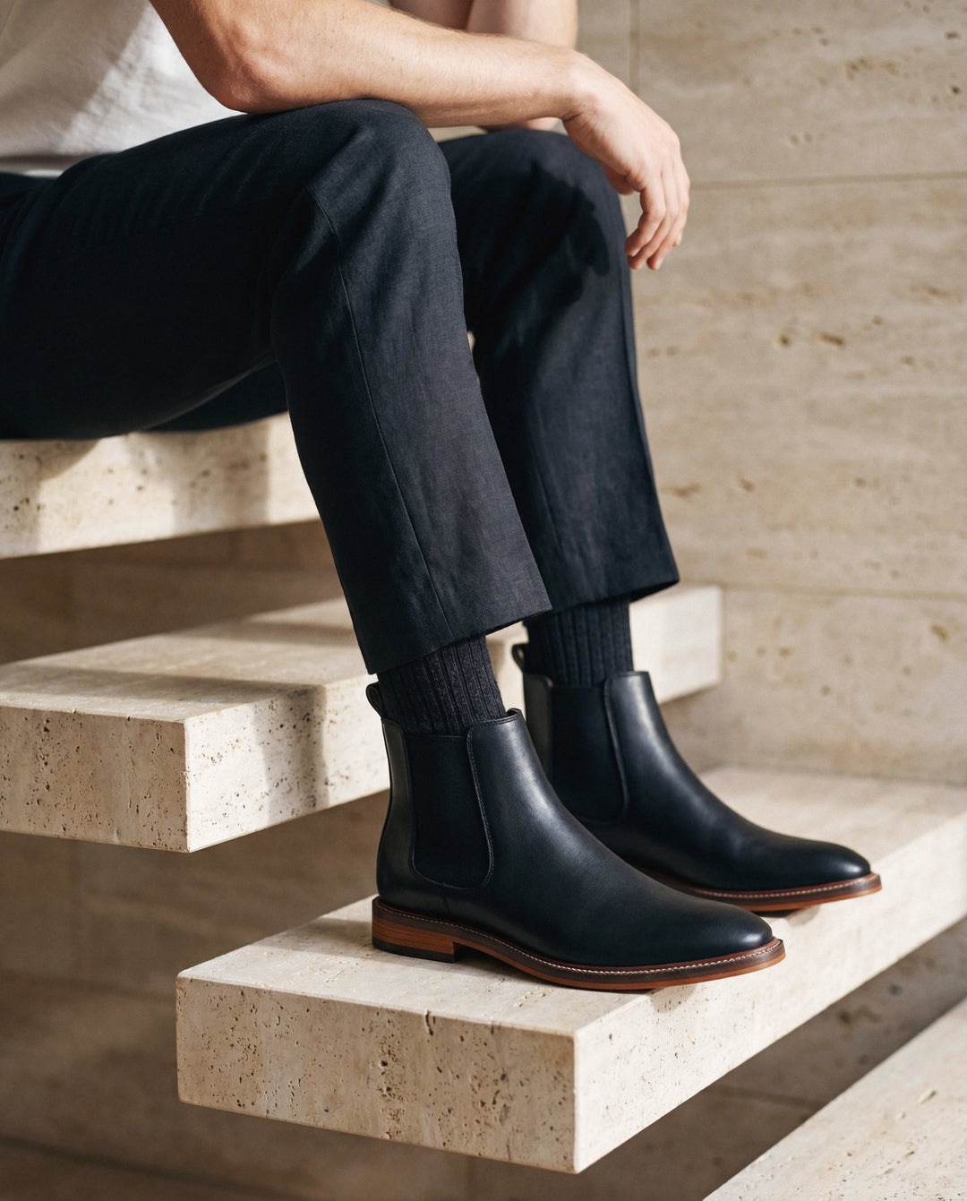 Person wearing black vegan leather boots sitting on stone steps.