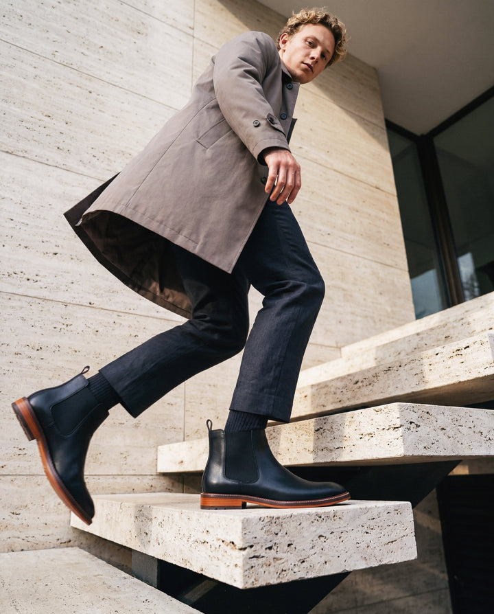 Man in a gray coat and black boots sitting on concrete steps.
