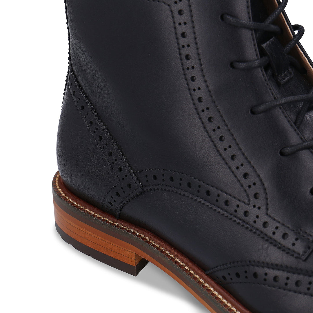 Black leather brogue shoe with brown sole on a white background