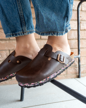 Charger l'image dans la galerie, Person wearing Nuoceans Nuos sustainable vegan clogs made from recycled ocean waste, dark brown colour, sitting outdoors against brick wall