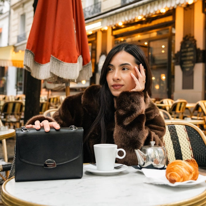 Sac Mini Paname Noir Lézard en cuir végétalien dans un café parisien avec un croissant pour la marque Ashoka Paris