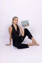 Load image into Gallery viewer, Sac bandoulière vegan bleu-gris effet lézard porté par une femme assise, style chic et responsable